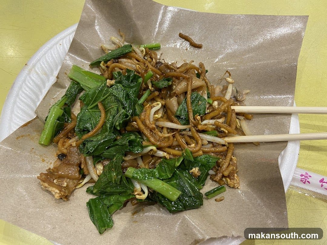 Chopsticks on a plate of stir-fried noodles and greens