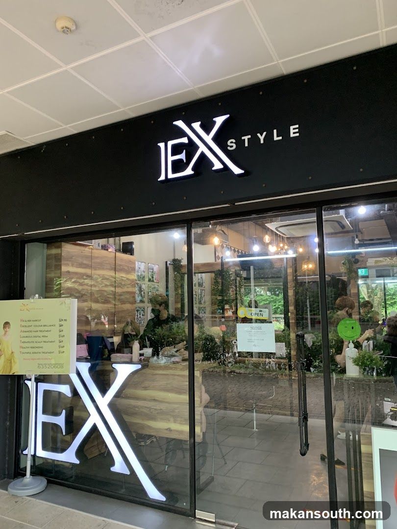 A modern shop front with a black facade featuring illuminated white 'JEX' and 'STYLE' signage above glass doors. Inside, visible through the windows, are plants, hanging lights, and a wooden table. A menu board stands outside near the entrance.
