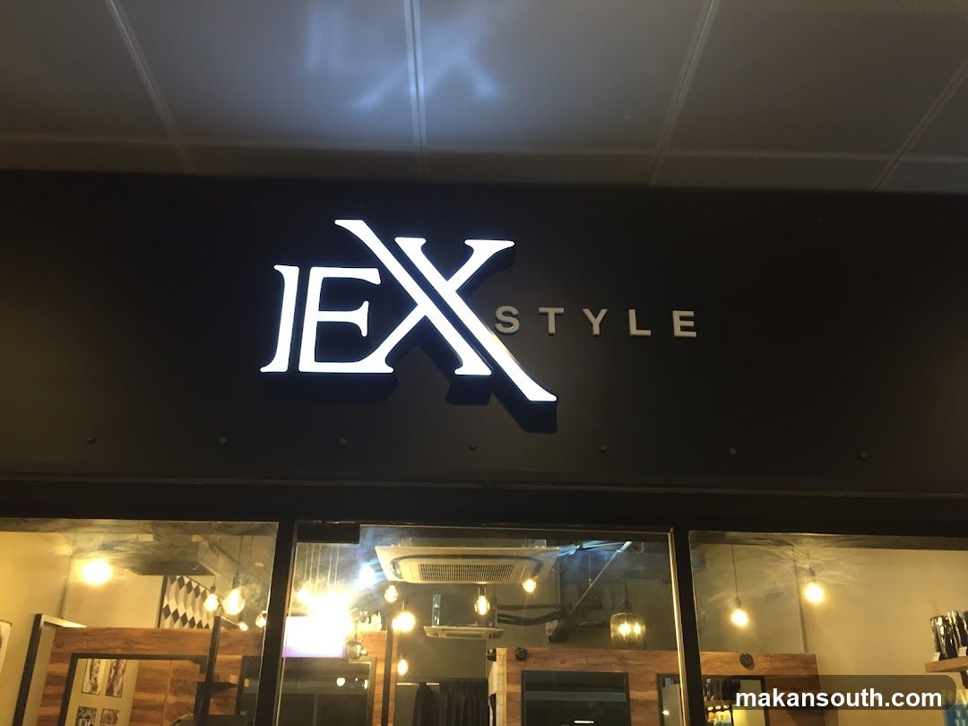 Night view of a shop entrance with illuminated signage reading 'JEX' in large stylized letters and 'STYLE' beside it. Below, glass doors reveal interior lighting and wooden paneling inside.