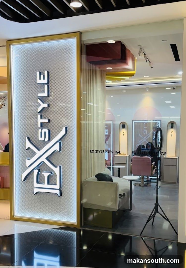 The image shows the exterior entrance of a shop named 'EX STYLE PRESTIGE'. A large, illuminated vertical sign with the logo 'EX STYLE' is mounted on the glass facade. Inside, through the transparent windows, one can see modern interior design elements including a white sofa, pink chairs, and decorative wall panels in shades of red and yellow. The floor inside appears to be tiled or polished concrete.