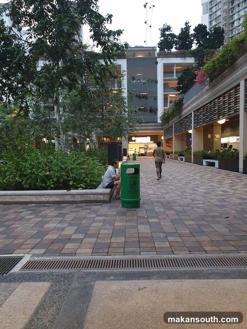 Outdoor plaza scene with green trash bin and seated person