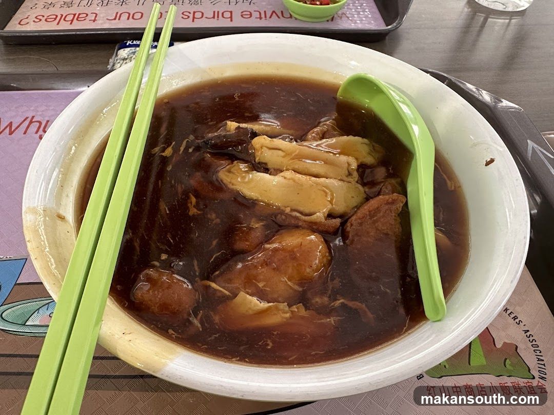Bowl of dark soup with chicken and green utensils