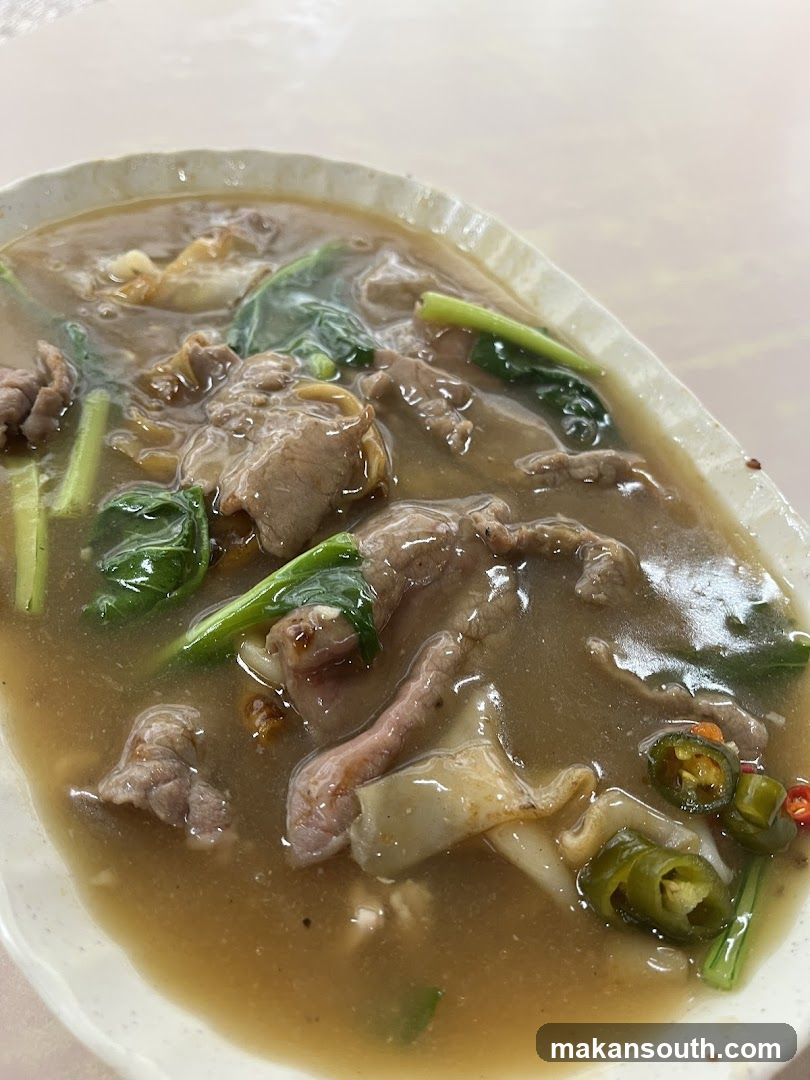 Bowl of Beef Noodle Soup with Greens and Chili Peppers