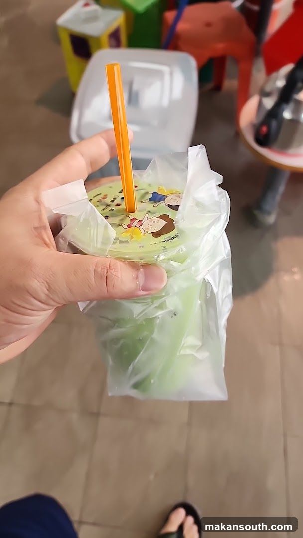 Hand holding a green drink in plastic wrap