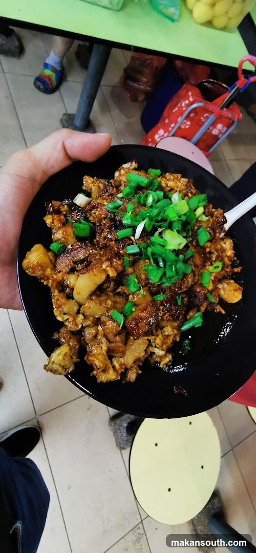 Hand holding a bowl of stir-fried rice with green onions