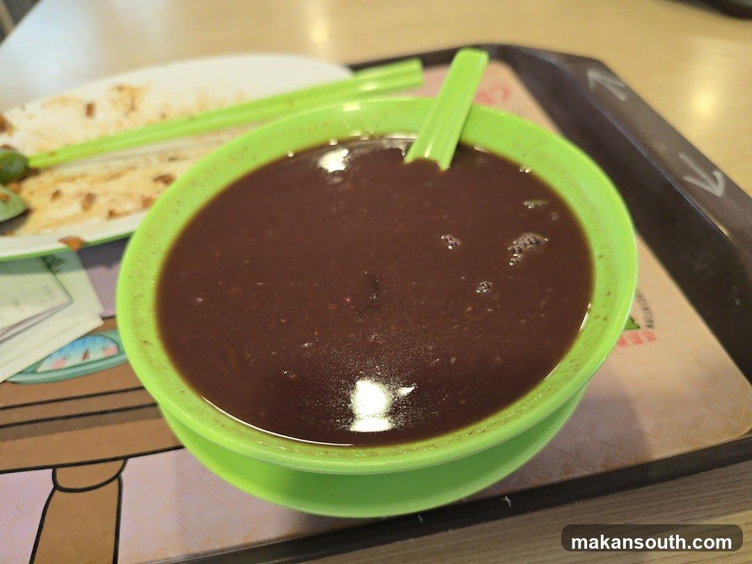 Bowl of dark soup with green spoon and chopsticks on tray
