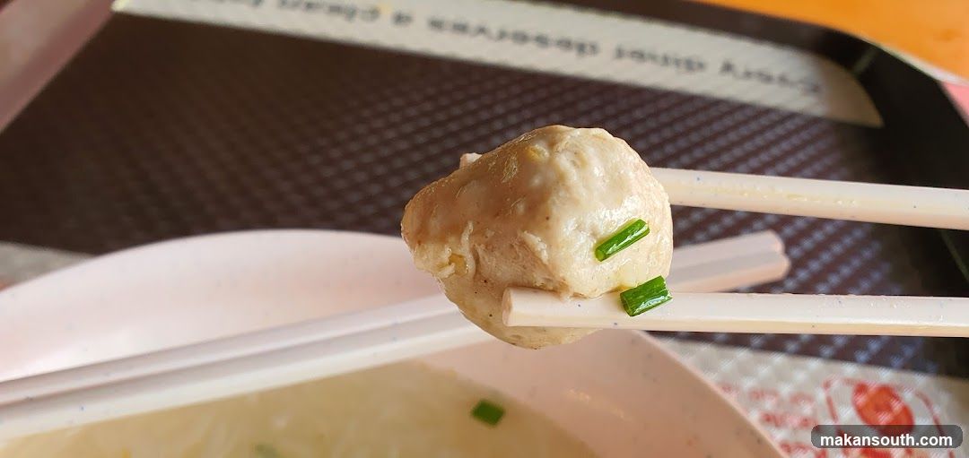 Chopsticks holding a meatball with green onions