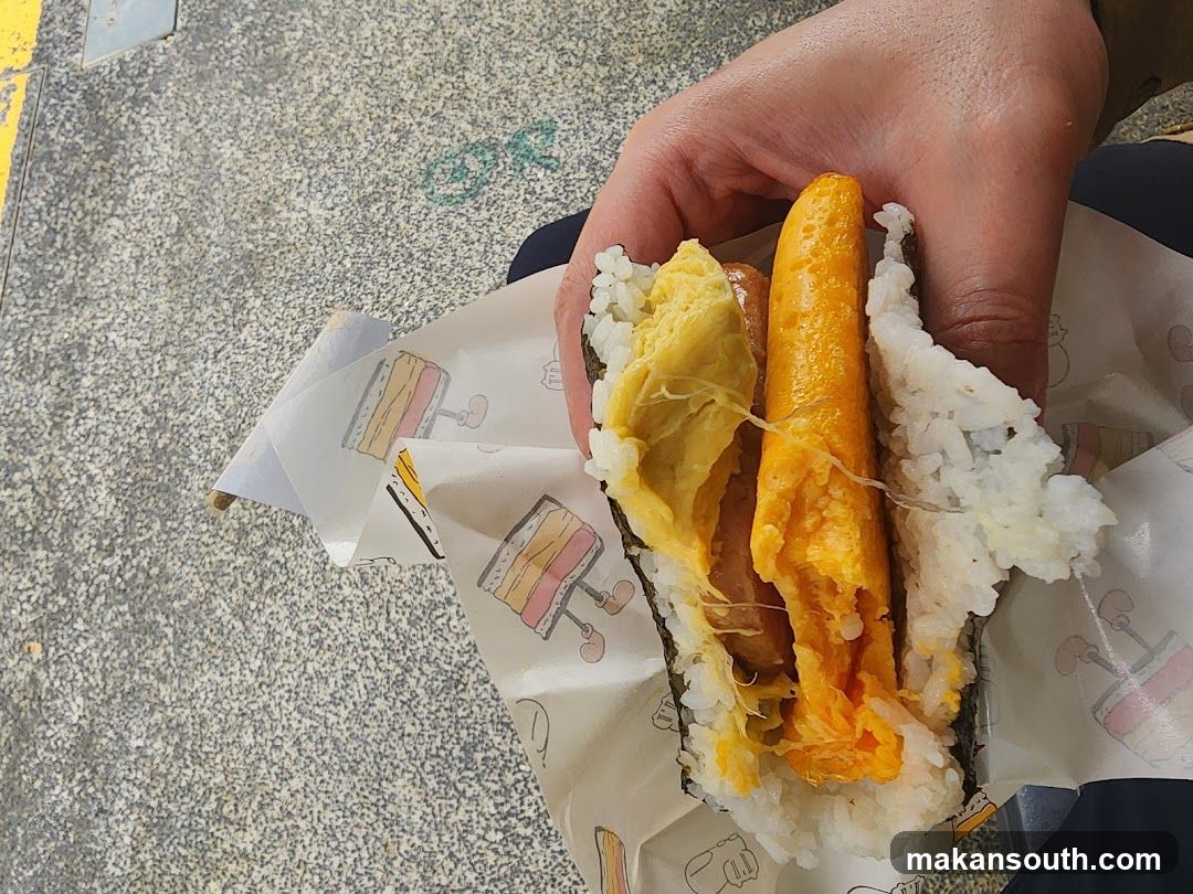 Hand holding a sushi roll with egg and sausage