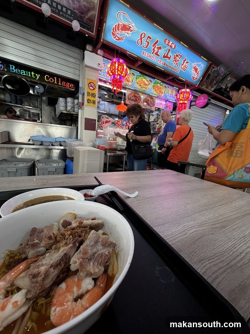 Food stall interior with customers and a bowl of noodles in foreground