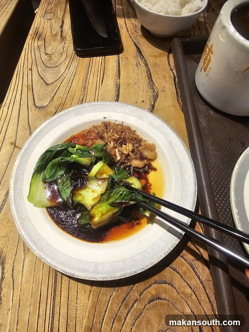 Dish with bok choy and fried garlic on wooden table