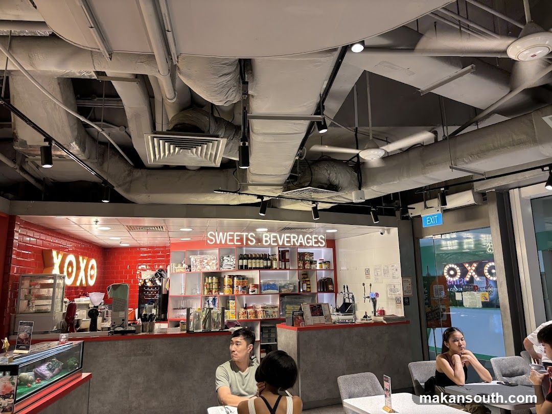 Interior of a cafe or shop with exposed ceiling pipes and shelves stocked with products.