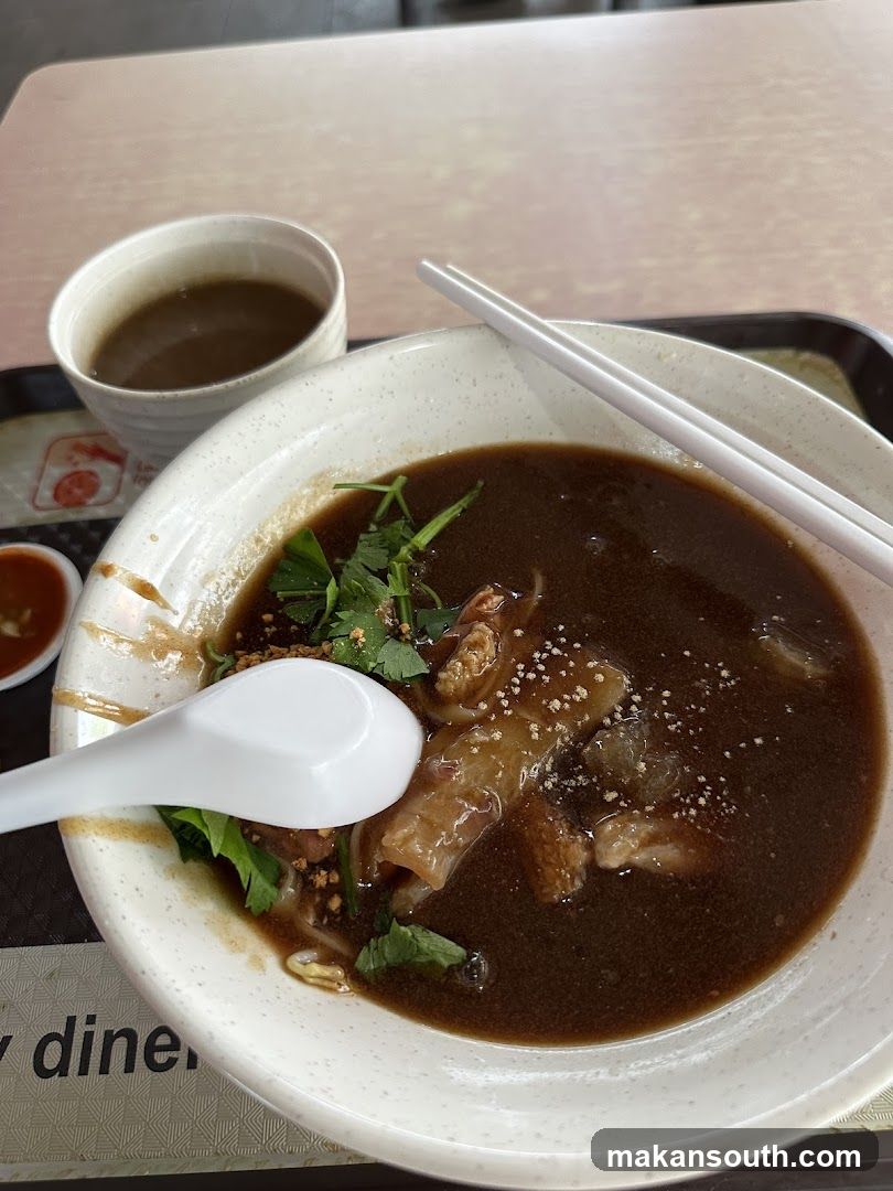 Bowl of Dark Broth Soup with Noodles and Garnish