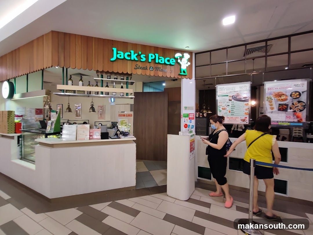 The exterior of a Jack's Place restaurant with a prominent sign. Inside, a counter displays food items, and promotional posters are visible. Two women are standing in line.