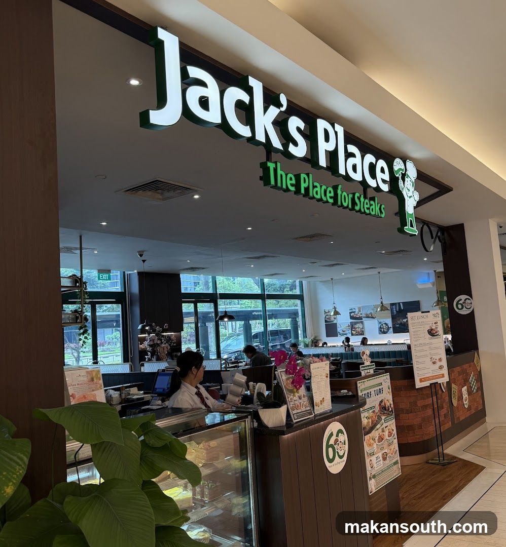 The exterior of a Jack's Place restaurant, with its prominent signage "Jack's Place The Place for Steaks" visible above the entrance. Inside, staff can be seen behind a counter, and diners are seated at tables. A display case with food items is also visible.