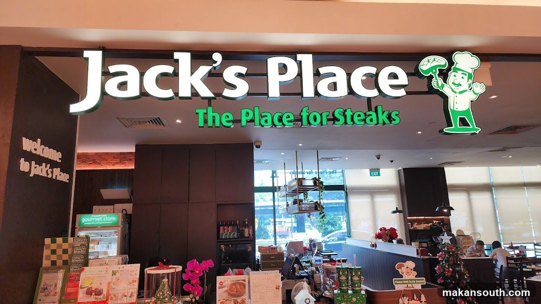 The exterior of a Jack's Place restaurant. A large sign above the entrance reads "Jack's Place The Place for Steaks" with a cartoon chef logo. To the left, a sign says "welcome to Jack's Place". Inside, a counter area is visible with a refrigerated display case labeled "gourmet store". There are also promotional flyers and a Christmas tree.