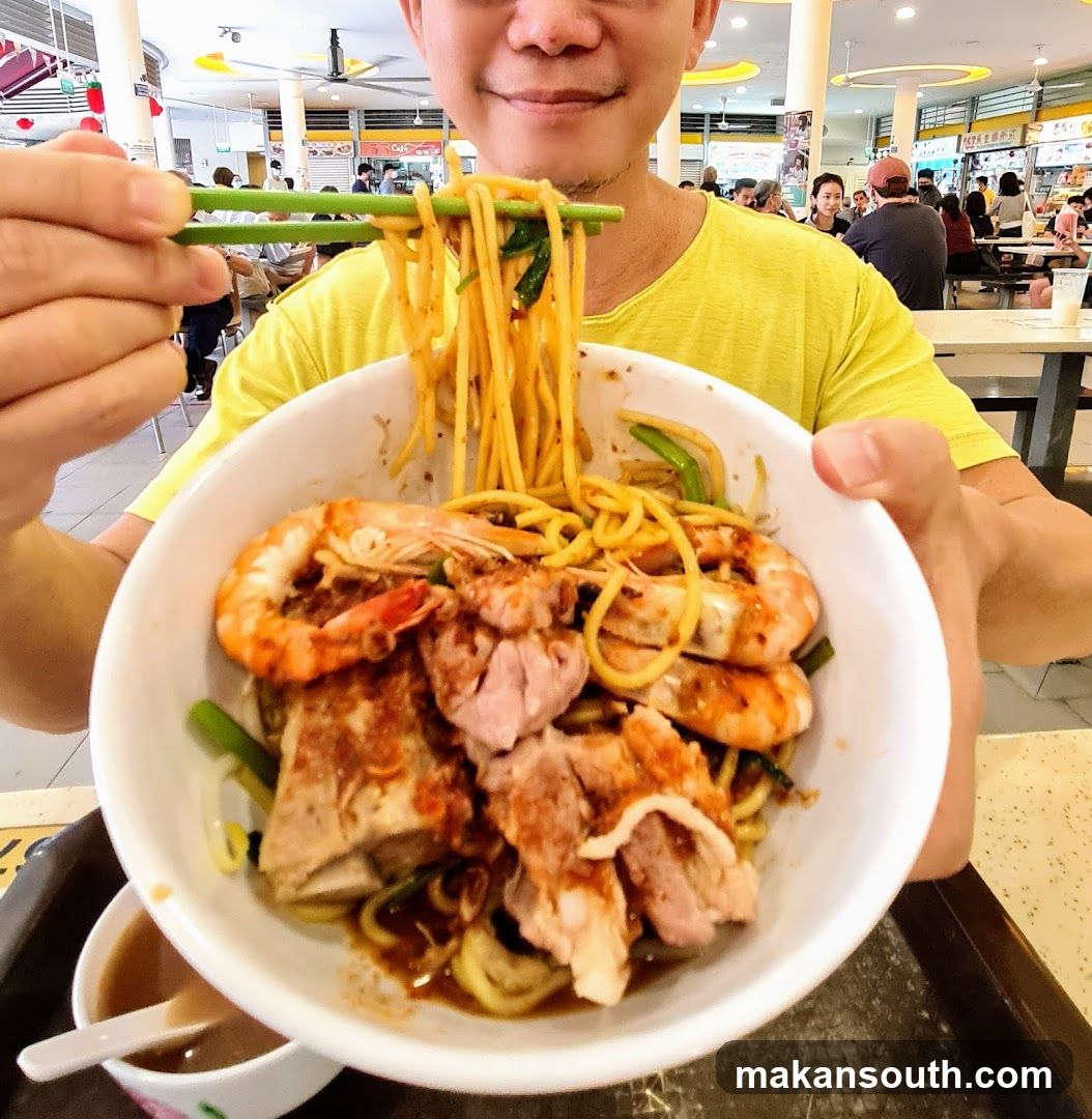 Person holding a bowl of noodles with shrimp and meat