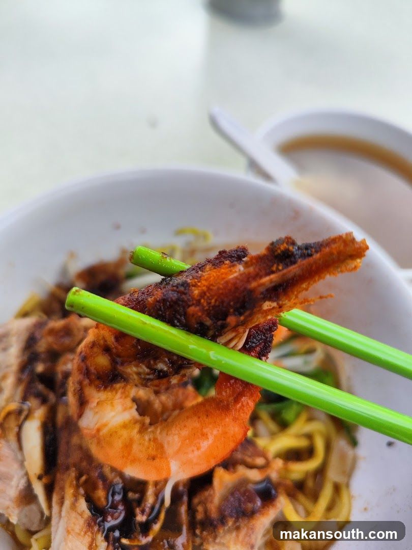 Close-up of a prawn being held by chopsticks over a bowl of noodles