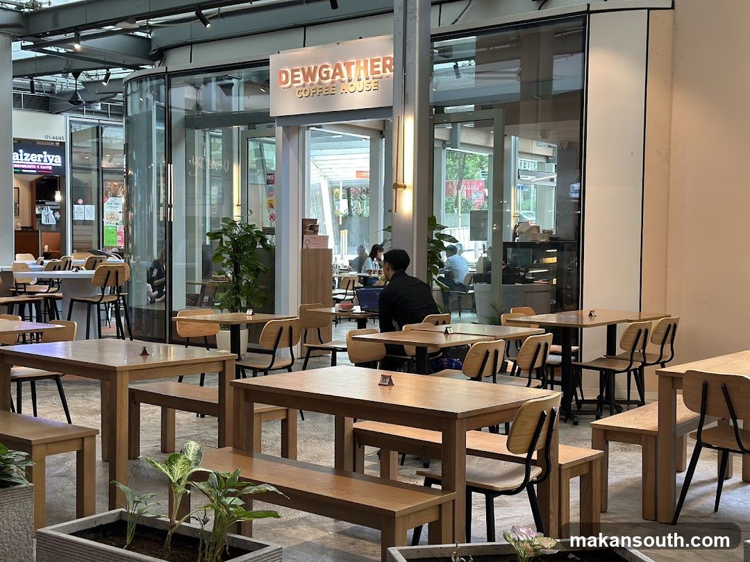 The exterior of a coffee house with large glass windows and doors. The sign above the entrance reads "DEWGATHER COFFEE HOUSE". Inside, tables and chairs are visible, along with some patrons.