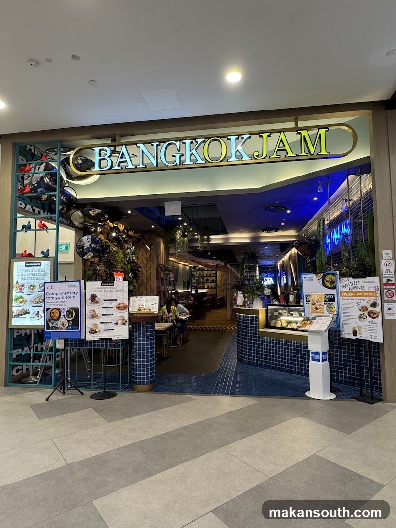 The exterior of a restaurant called Bangkok Jam. The restaurant has a large sign with the name in illuminated letters. There are menus displayed outside the entrance.