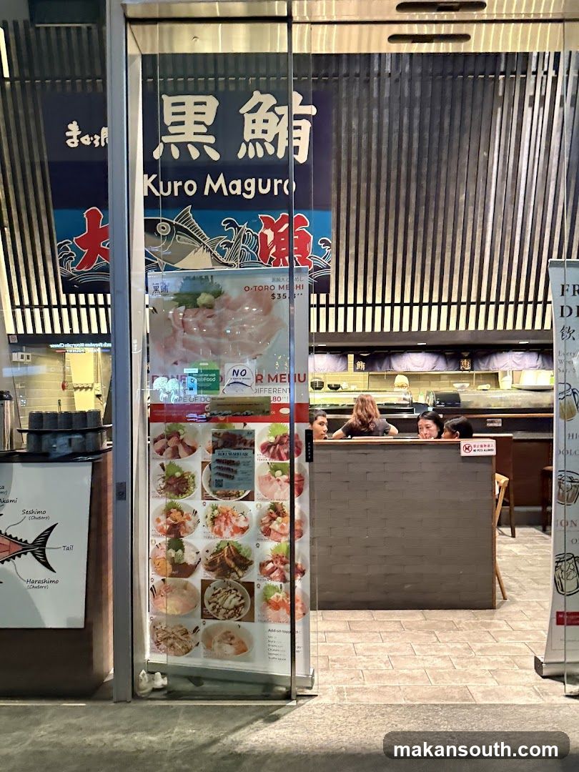 The exterior of a Japanese restaurant with a prominent sign reading "Kuro Maguro" in English and Japanese characters. A glass door displays a menu with various dishes, primarily featuring tuna and sashimi. Inside, staff members are visible behind a counter.