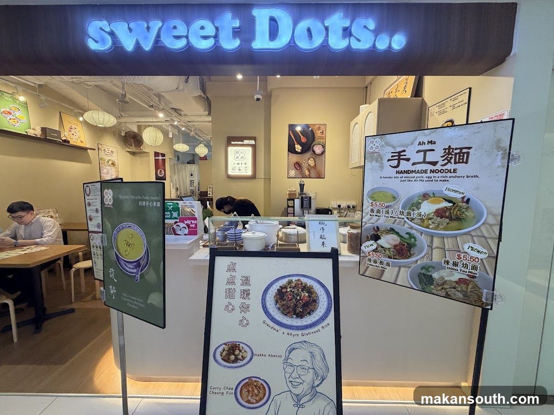 A storefront with a neon sign that says "sweet Dots..". There are menus displayed outside the shop. Inside, a person is working behind the counter.