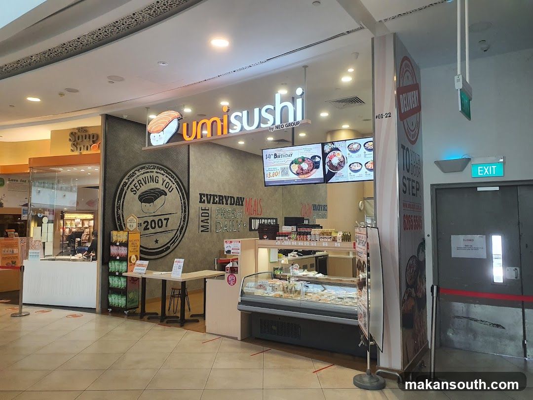 The exterior of a Umi Sushi restaurant. The restaurant has a large sign with the Umi Sushi logo and name. There is also a menu board displaying various dishes and prices. The restaurant is located next to "The Soup Spoon".
