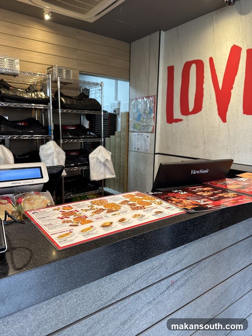 The exterior of a Pizza Hut restaurant with its prominent signage. There are promotional banners outside the entrance, one advertising careers and another promoting a "My Box" meal deal. Inside, tables and chairs are visible, along with the counter area.
