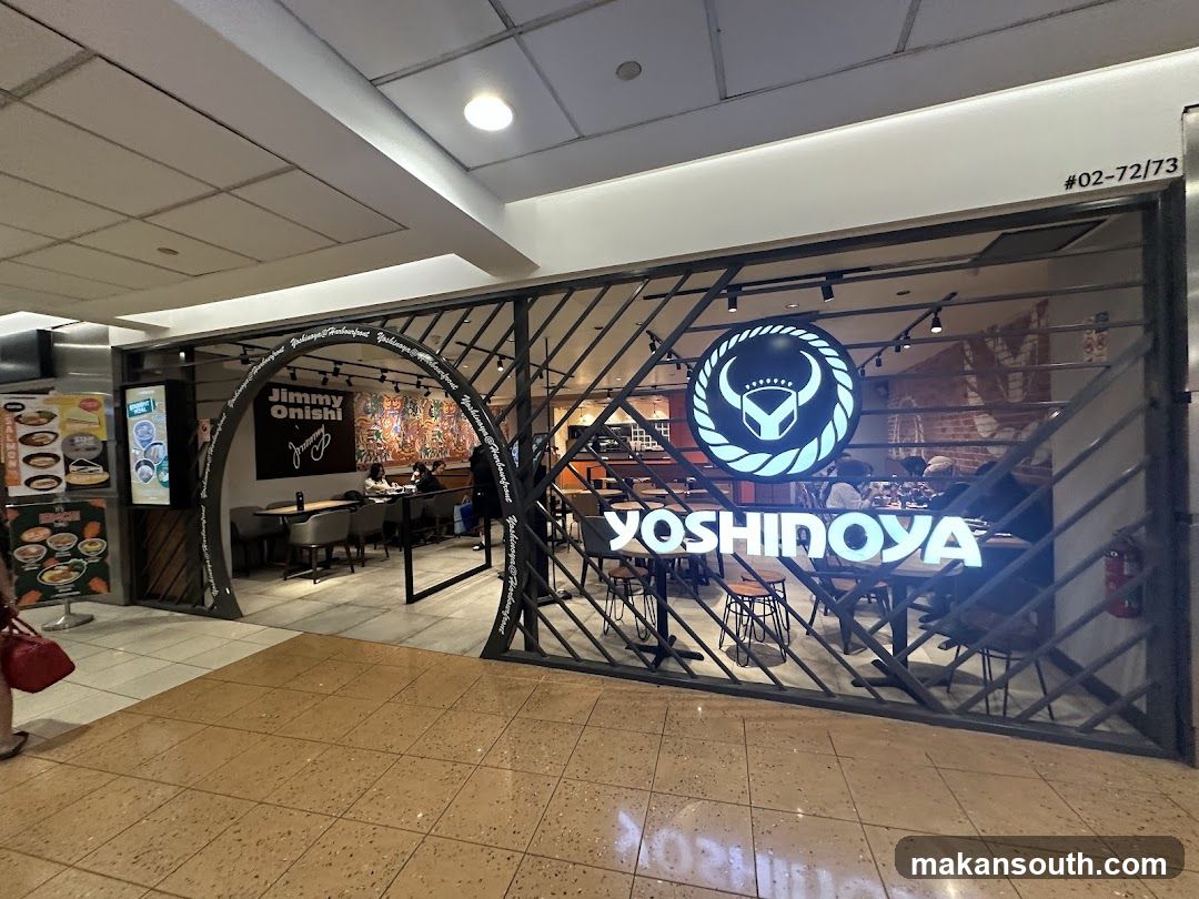 The exterior of a Yoshinoya restaurant with a distinctive archway entrance. The Yoshinoya logo is prominently displayed on the facade. Inside, tables and chairs are visible, with patrons seated. To the left, a menu board displays various food items.
