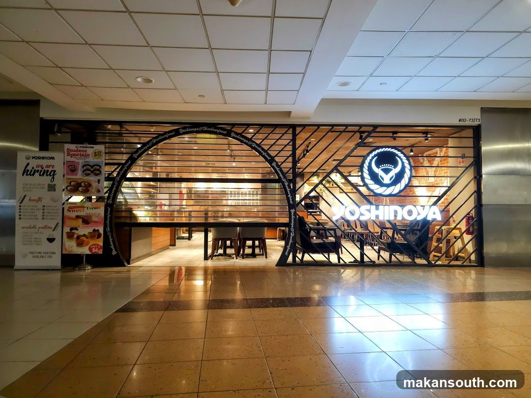 The storefront of a Yoshinoya restaurant is visible, with its logo and name prominently displayed. The entrance is partially obscured by a metal grate. To the left of the entrance, there is a "We are hiring" poster.