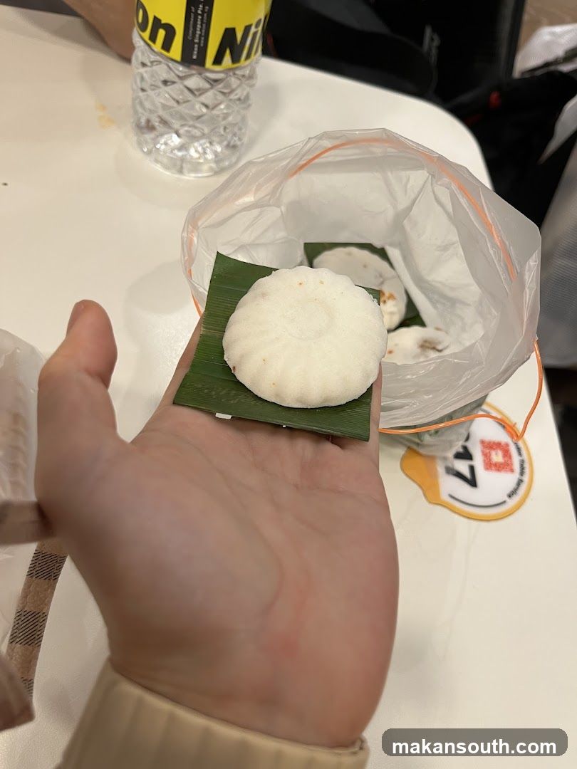 Hand holding a small white pastry on a banana leaf