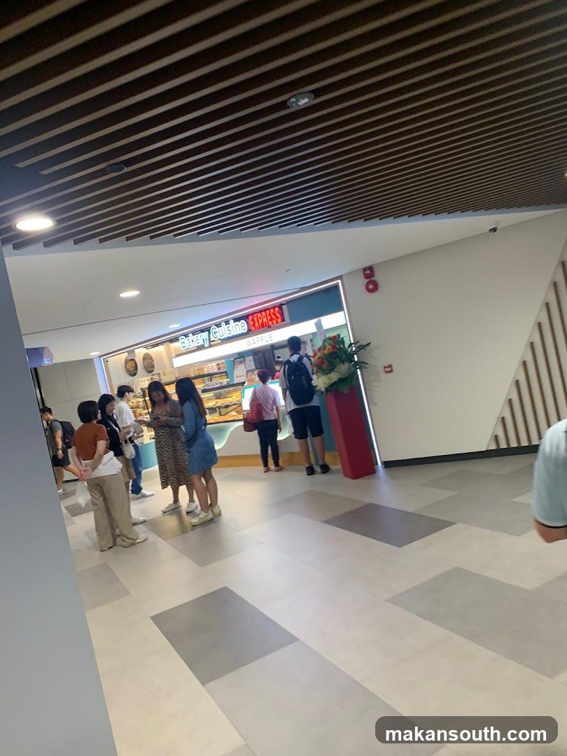 A view of the exterior of a bakery with a sign that reads "Bakery Cuisine EXPRESS" and "WAFFLE". There are people standing in front of the counter, and display cases filled with baked goods.