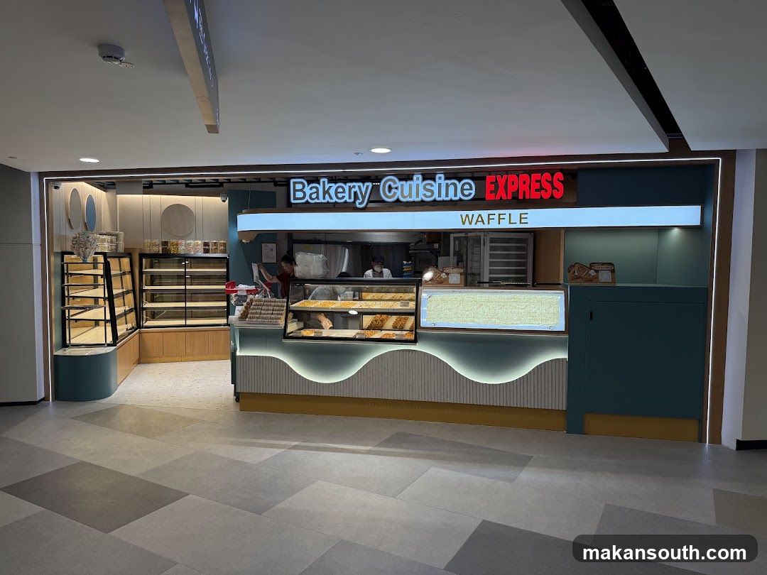 A bakery counter with display cases filled with pastries and baked goods. The signage above reads "Bakery Cuisine EXPRESS" and "WAFFLE". There are empty shelves to the left and a service counter with staff behind it.