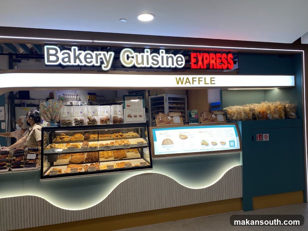A bakery counter with a display case full of pastries and baked goods. Above the counter, a sign reads "Bakery Cuisine EXPRESS" and "WAFFLE". There are also menus displayed with waffle options.