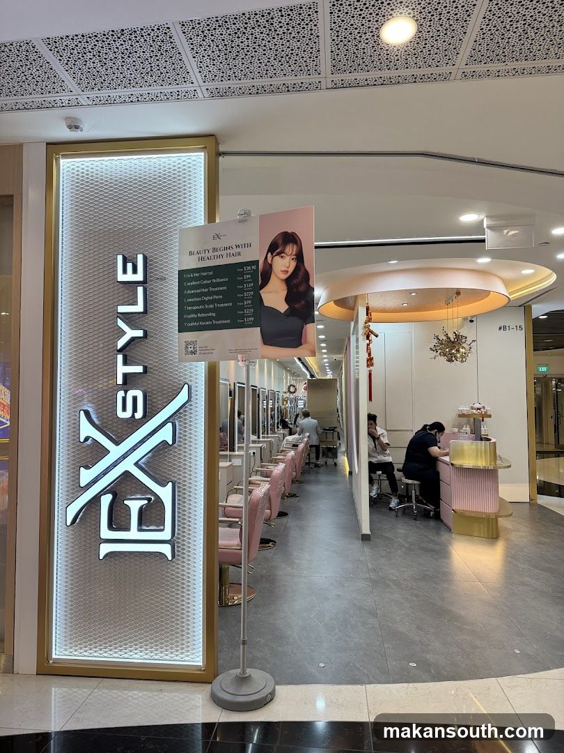 A brightly lit hair salon with a prominent vertical sign displaying "EX STYLE". Pink salon chairs are arranged in a row, and a menu board is displayed near the entrance. Two staff members are visible inside, one attending to a client at a reception desk.